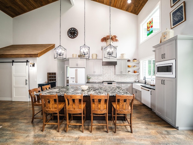 kitchen featuring appliances with stainless steel finishes, gray cabinetry, high vaulted ceiling, a barn door, and a kitchen island