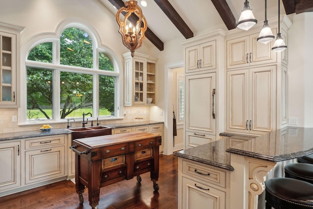 kitchen featuring lofted ceiling with beams, dark stone countertops, hanging light fixtures, and a wealth of natural light