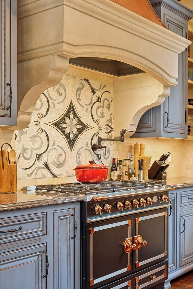 kitchen featuring custom range hood, backsplash, stone countertops, and range with two ovens