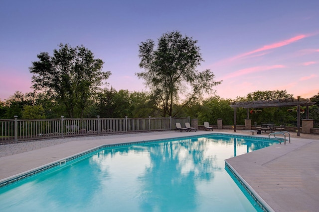 pool at dusk with a patio area and a pergola