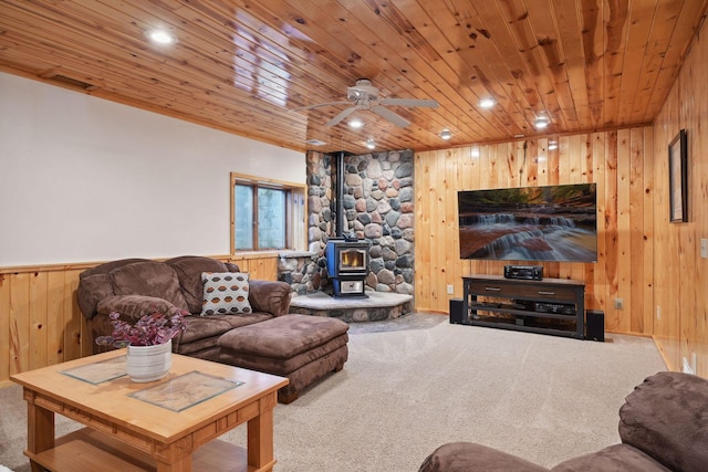 living room featuring ceiling fan, a wood stove, wooden ceiling, and carpet floors