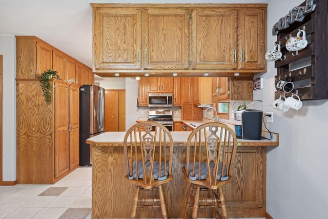 kitchen with appliances with stainless steel finishes, a kitchen bar, kitchen peninsula, and light tile patterned floors