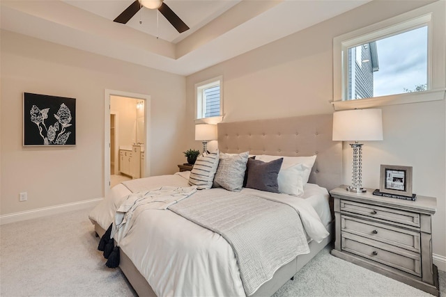 carpeted bedroom with ceiling fan, ensuite bathroom, and a raised ceiling