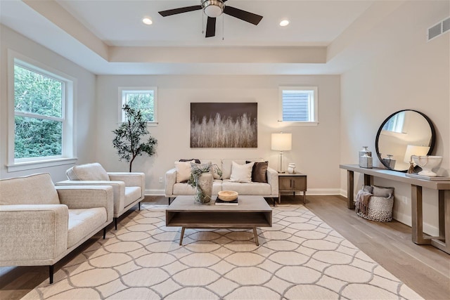 living room with light hardwood / wood-style floors, a tray ceiling, and ceiling fan