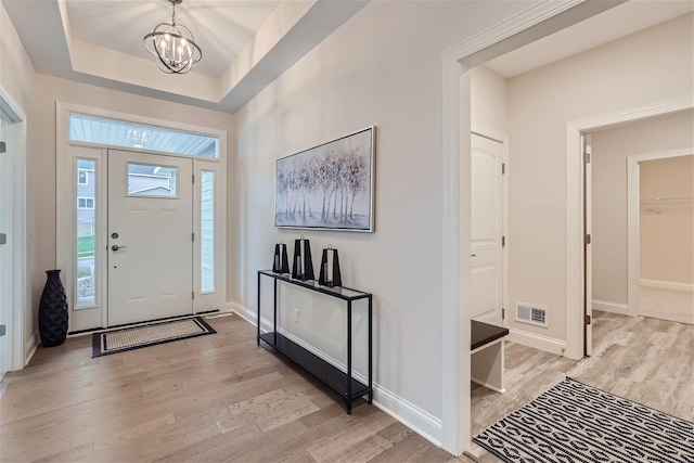 entryway with a notable chandelier, a raised ceiling, and light hardwood / wood-style floors