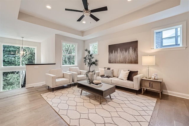 living room featuring ceiling fan with notable chandelier, a raised ceiling, and hardwood / wood-style floors