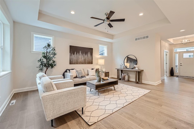 living room featuring light wood-type flooring, ceiling fan with notable chandelier, and a raised ceiling