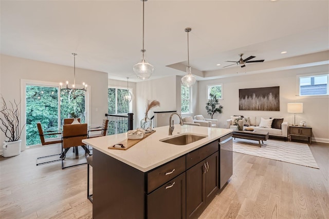 kitchen with an island with sink, light hardwood / wood-style floors, sink, hanging light fixtures, and stainless steel dishwasher