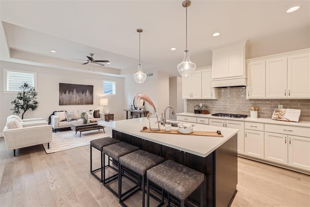 kitchen featuring hanging light fixtures, light wood-type flooring, white cabinetry, a kitchen bar, and a center island with sink