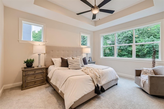 carpeted bedroom with multiple windows, ceiling fan, and a raised ceiling