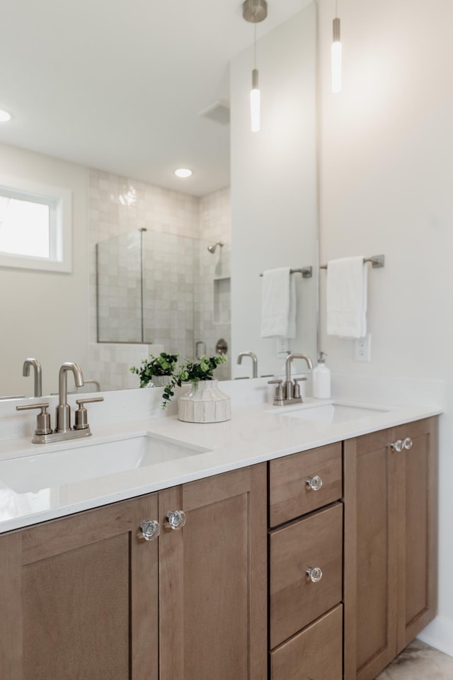 bathroom with a tile shower, double vanity, and a sink