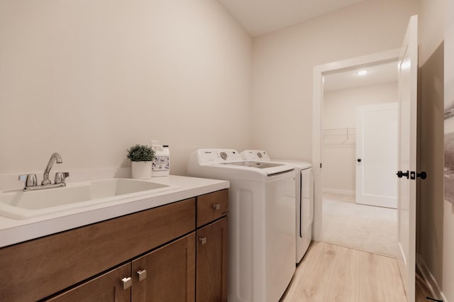 laundry area featuring light wood-style floors, independent washer and dryer, cabinet space, and a sink