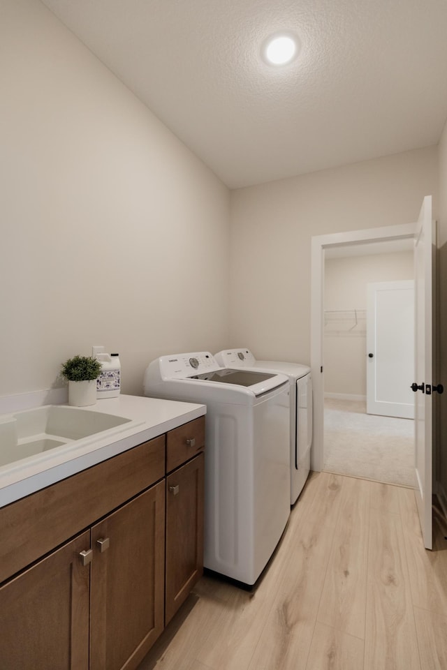 laundry area with cabinet space, a textured ceiling, light wood finished floors, and separate washer and dryer