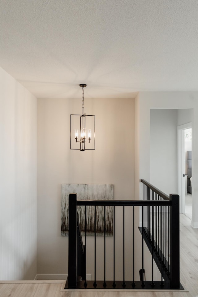 stairs featuring a textured ceiling, wood finished floors, and an inviting chandelier