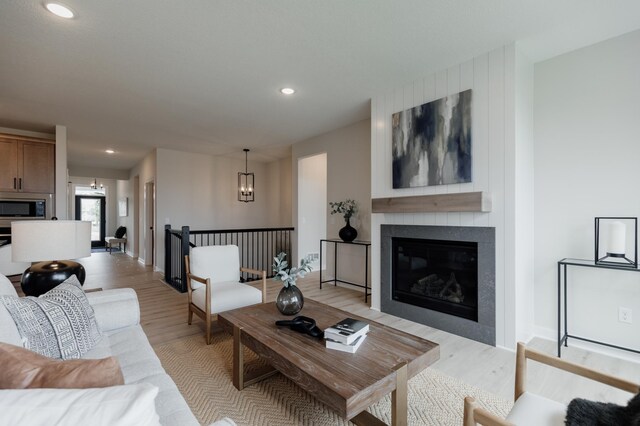 living area with baseboards, a tiled fireplace, light wood-type flooring, a chandelier, and recessed lighting