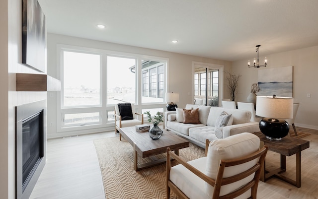 living room featuring a chandelier, light wood-type flooring, a glass covered fireplace, and recessed lighting