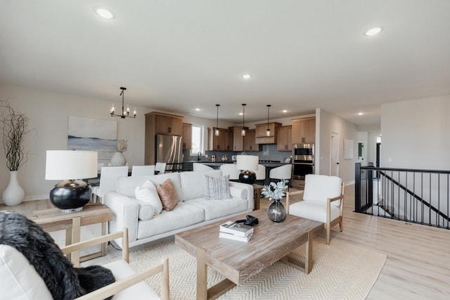 living room featuring baseboards, recessed lighting, light wood-type flooring, and an inviting chandelier