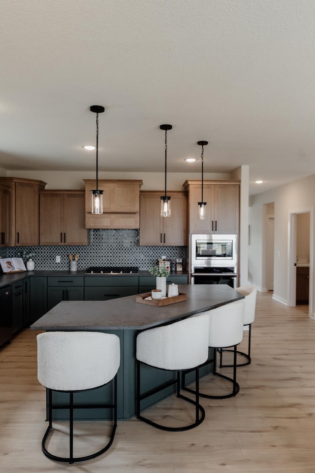 kitchen featuring stovetop, dark countertops, backsplash, and light wood-style floors