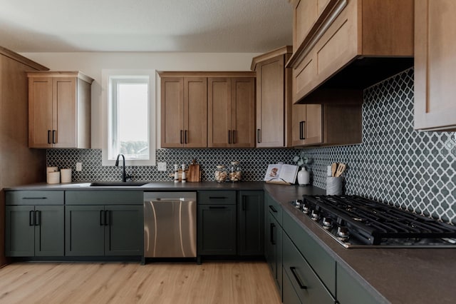 kitchen with light wood finished floors, custom exhaust hood, stainless steel appliances, dark countertops, and a sink