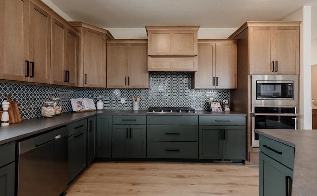 kitchen with light wood-type flooring, dark countertops, stainless steel appliances, and decorative backsplash