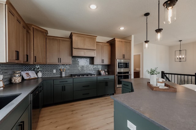 kitchen with light wood-style flooring, stainless steel appliances, decorative backsplash, dark countertops, and decorative light fixtures