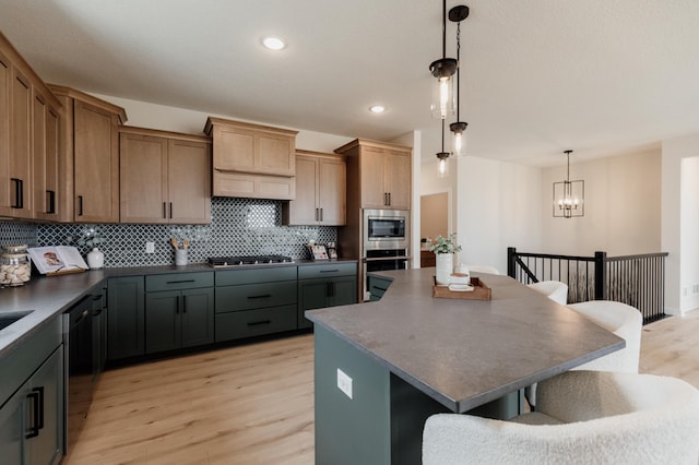 kitchen featuring decorative light fixtures, tasteful backsplash, dark countertops, light wood-style flooring, and appliances with stainless steel finishes