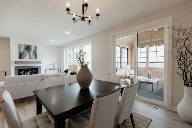 dining space featuring light wood-style floors, visible vents, a wealth of natural light, and a glass covered fireplace