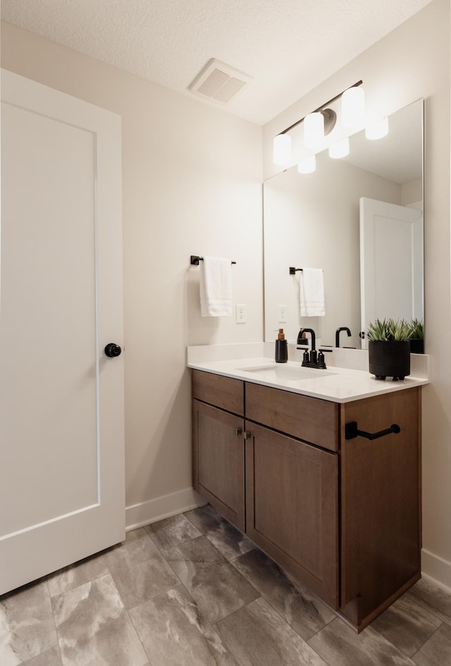 bathroom featuring baseboards, visible vents, a textured ceiling, and vanity