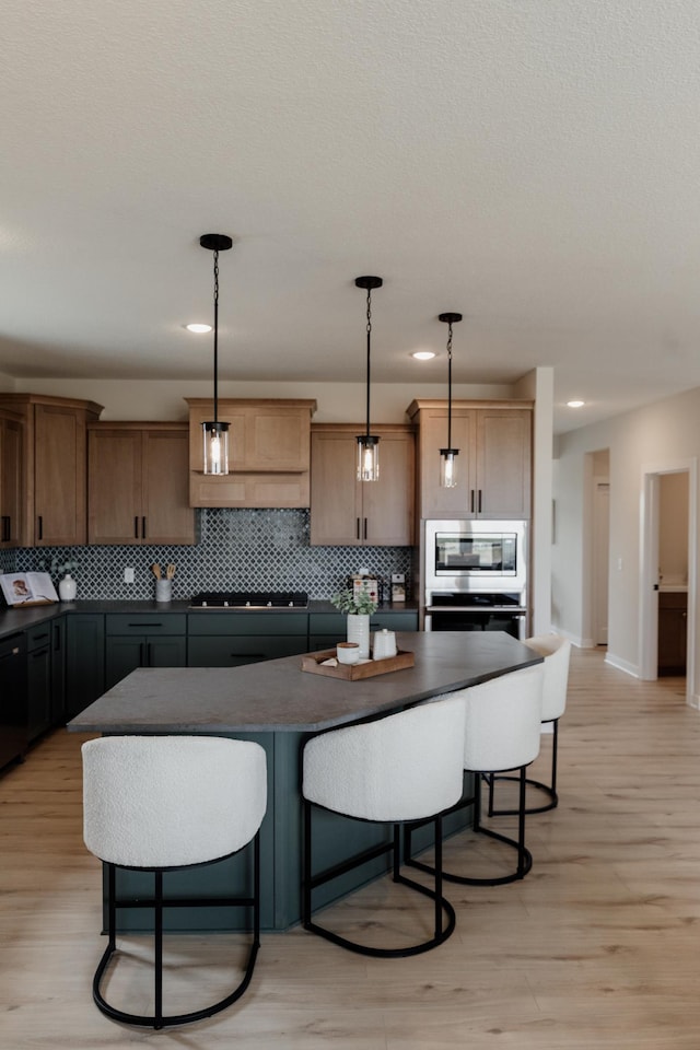 kitchen featuring stovetop, dark countertops, backsplash, and stainless steel oven