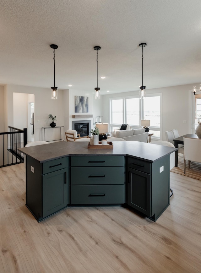 kitchen featuring a glass covered fireplace, open floor plan, a kitchen island, light wood-style floors, and pendant lighting