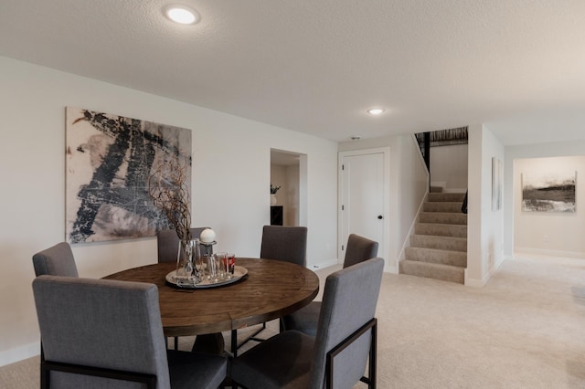 dining space featuring a textured ceiling, light colored carpet, recessed lighting, stairway, and baseboards