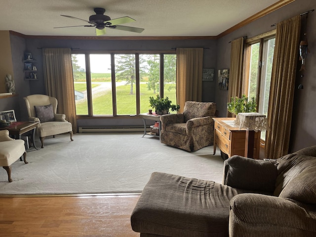 living area featuring crown molding, baseboard heating, ceiling fan, a textured ceiling, and light hardwood / wood-style floors