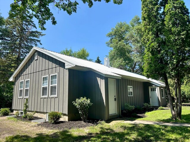 exterior space featuring board and batten siding, a yard, metal roof, and a chimney