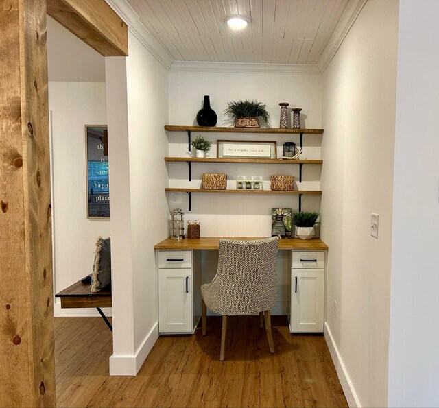 home office with built in study area, crown molding, and wood finished floors