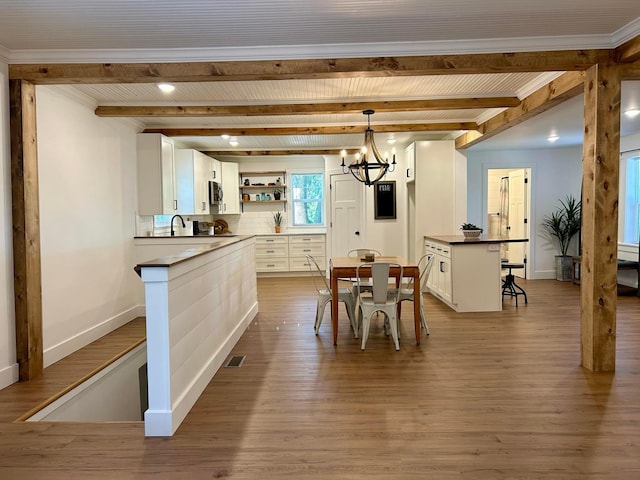 dining room with light hardwood / wood-style floors, crown molding, a notable chandelier, and beamed ceiling