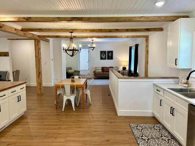 kitchen featuring butcher block counters, beam ceiling, open floor plan, white cabinetry, and a sink