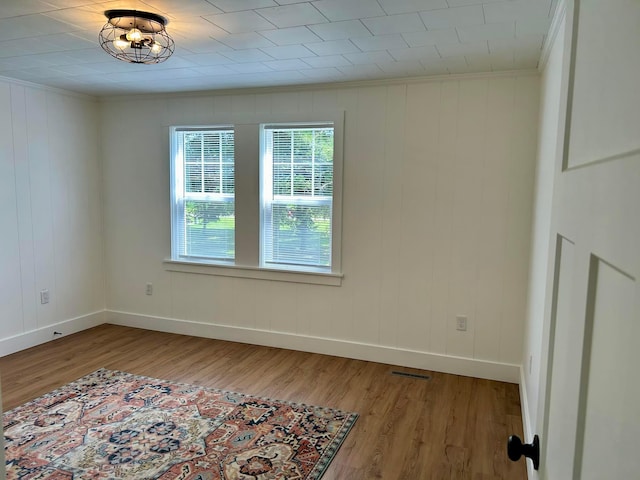 empty room featuring ornamental molding, hardwood / wood-style flooring, and wood walls