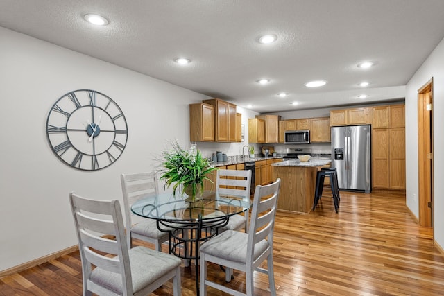 dining space with sink, a textured ceiling, and light hardwood / wood-style flooring