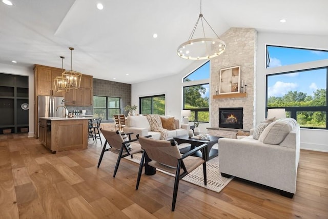 living room with light wood-style flooring, an inviting chandelier, a stone fireplace, high vaulted ceiling, and recessed lighting