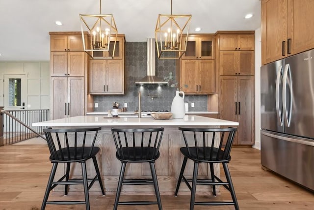 kitchen featuring an inviting chandelier, wall chimney exhaust hood, light countertops, and freestanding refrigerator