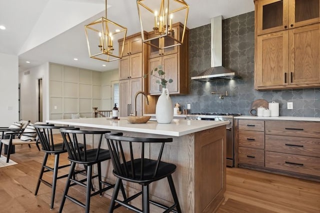 kitchen featuring a center island with sink, light wood finished floors, stainless steel stove, a sink, and wall chimney range hood