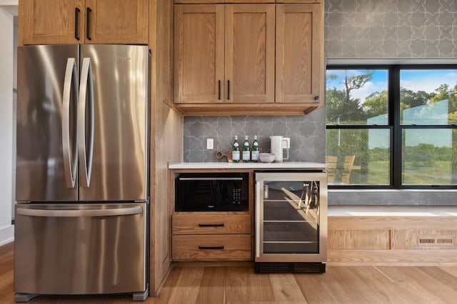 kitchen featuring black microwave, wine cooler, wood finished floors, freestanding refrigerator, and brown cabinetry