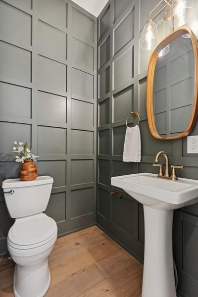 half bath featuring toilet, a decorative wall, and wood finished floors