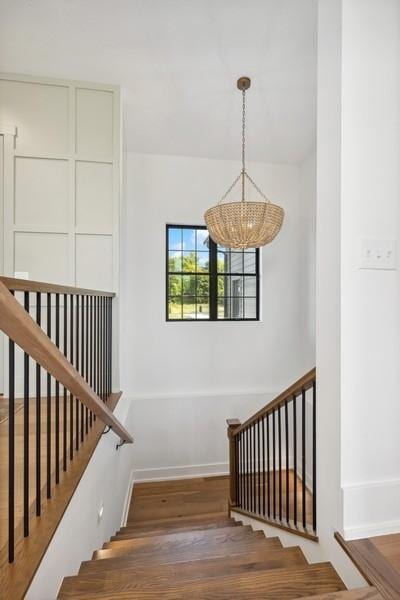 stairway with baseboards, a chandelier, and wood finished floors