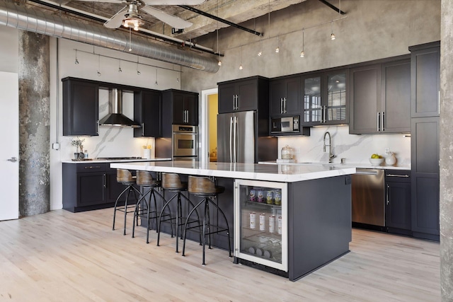 kitchen with wall chimney exhaust hood, a center island, light hardwood / wood-style flooring, appliances with stainless steel finishes, and ceiling fan