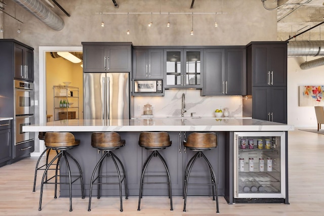 kitchen with appliances with stainless steel finishes, sink, wine cooler, a kitchen breakfast bar, and a large island