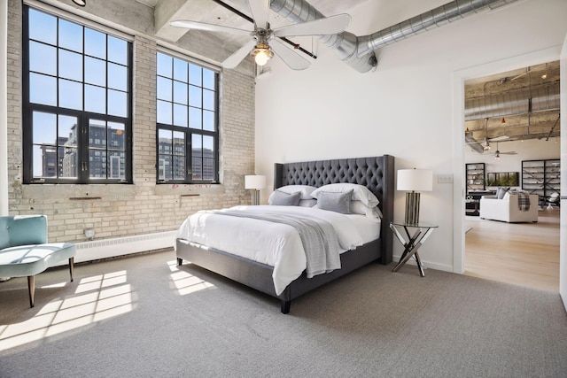 carpeted bedroom featuring a high ceiling, a baseboard radiator, brick wall, and ceiling fan