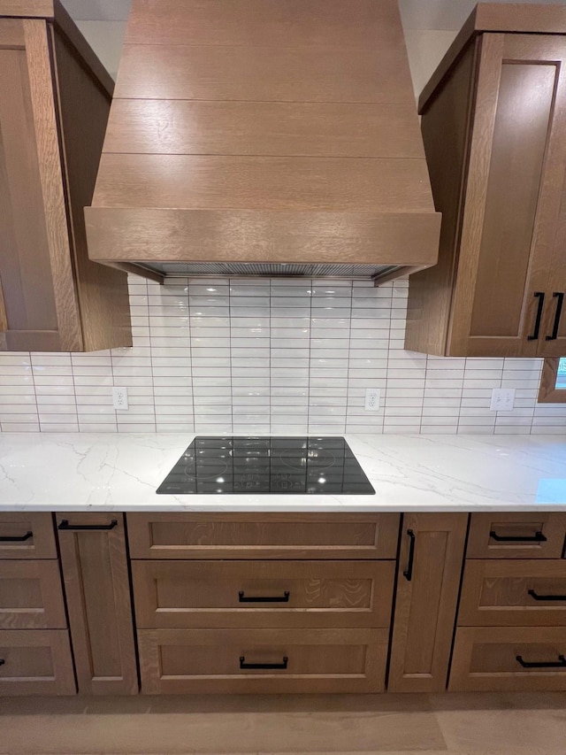 kitchen featuring custom exhaust hood, tasteful backsplash, black electric cooktop, and light stone counters