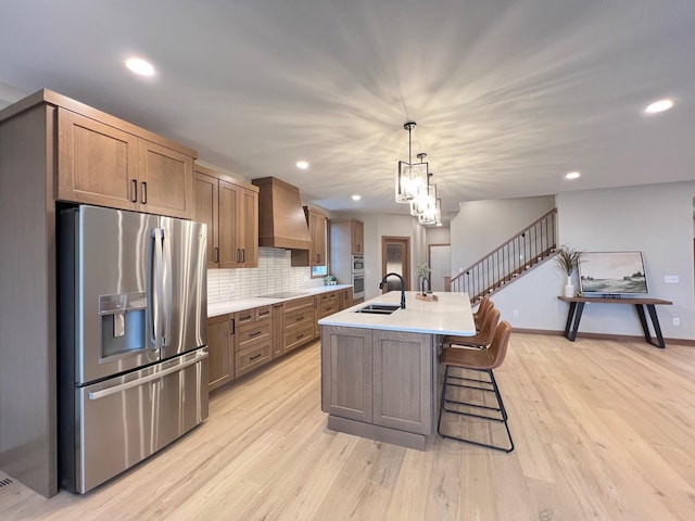 kitchen with sink, stainless steel appliances, a center island with sink, decorative light fixtures, and custom exhaust hood