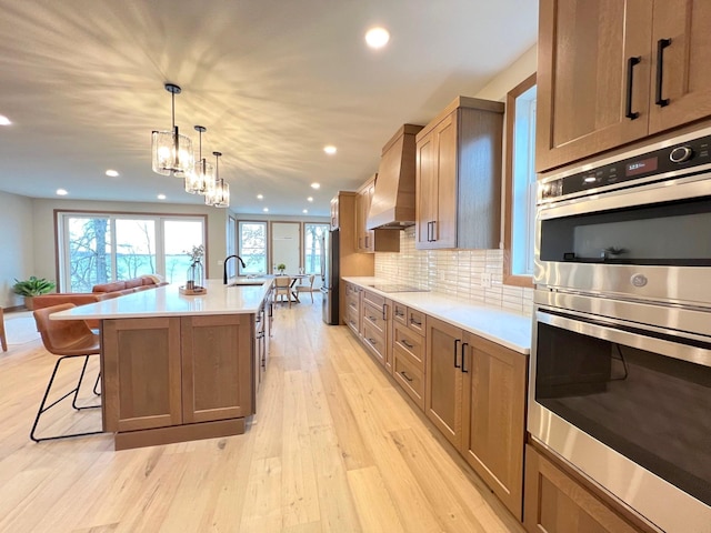 kitchen with premium range hood, a kitchen island with sink, stainless steel appliances, tasteful backsplash, and a kitchen bar